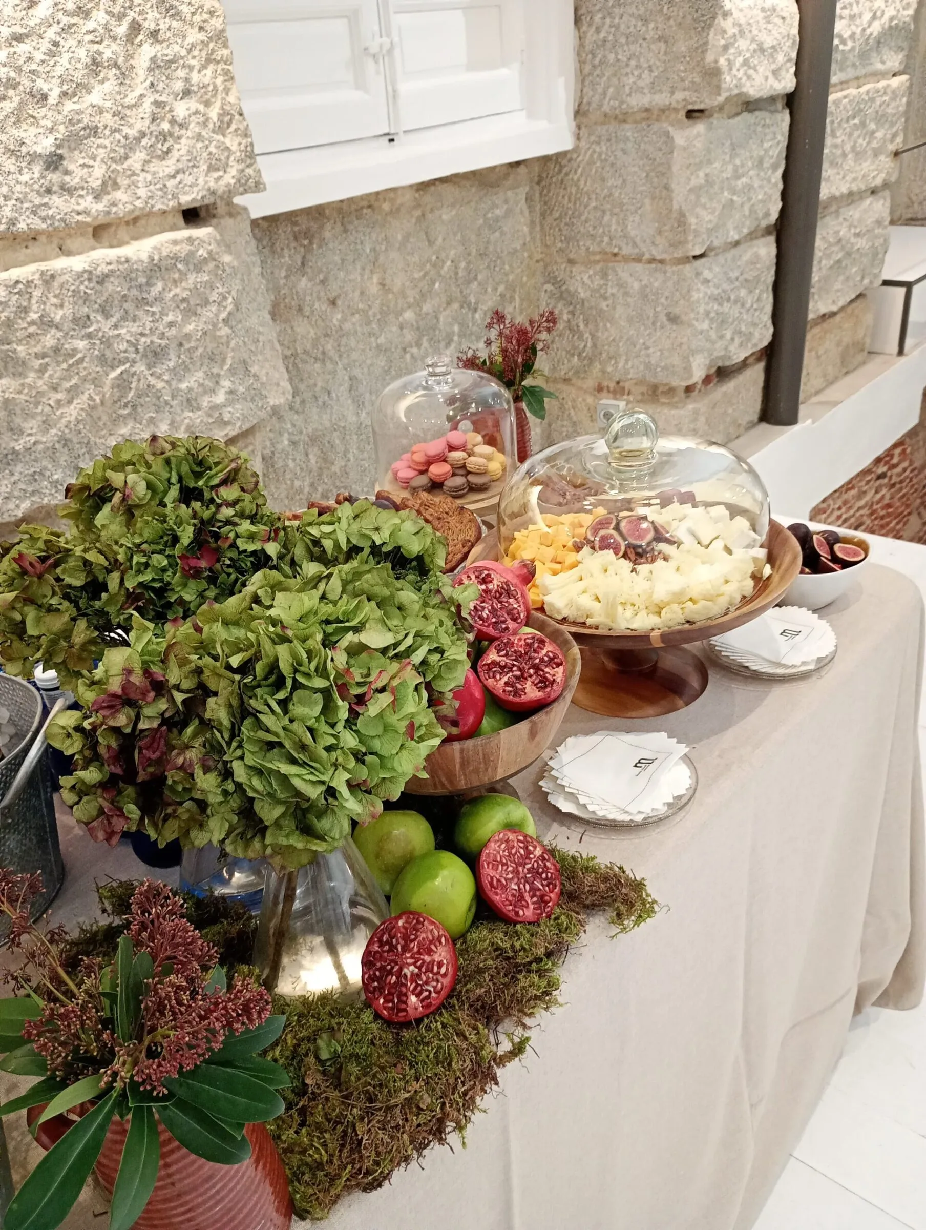 Mesa de buffet con quesos, granadas, higos, macarons y hortensias en un evento de otoño, María Lluch Catering en Madrid