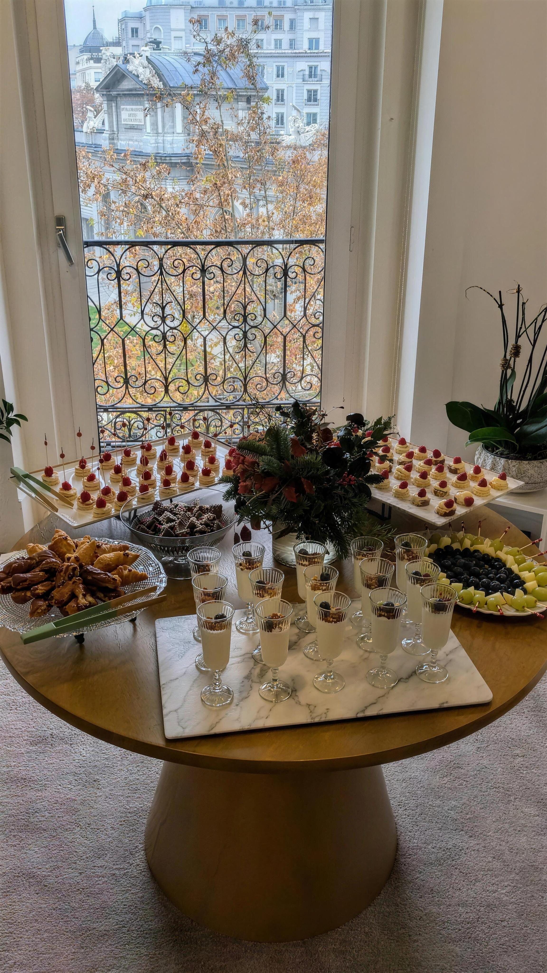 Mesa navideña de desayuno con pinchos, vasitos de yogur con granola y bollería, con vistas a la Puerta de Alcalá, catering de María Lluch en Madrid