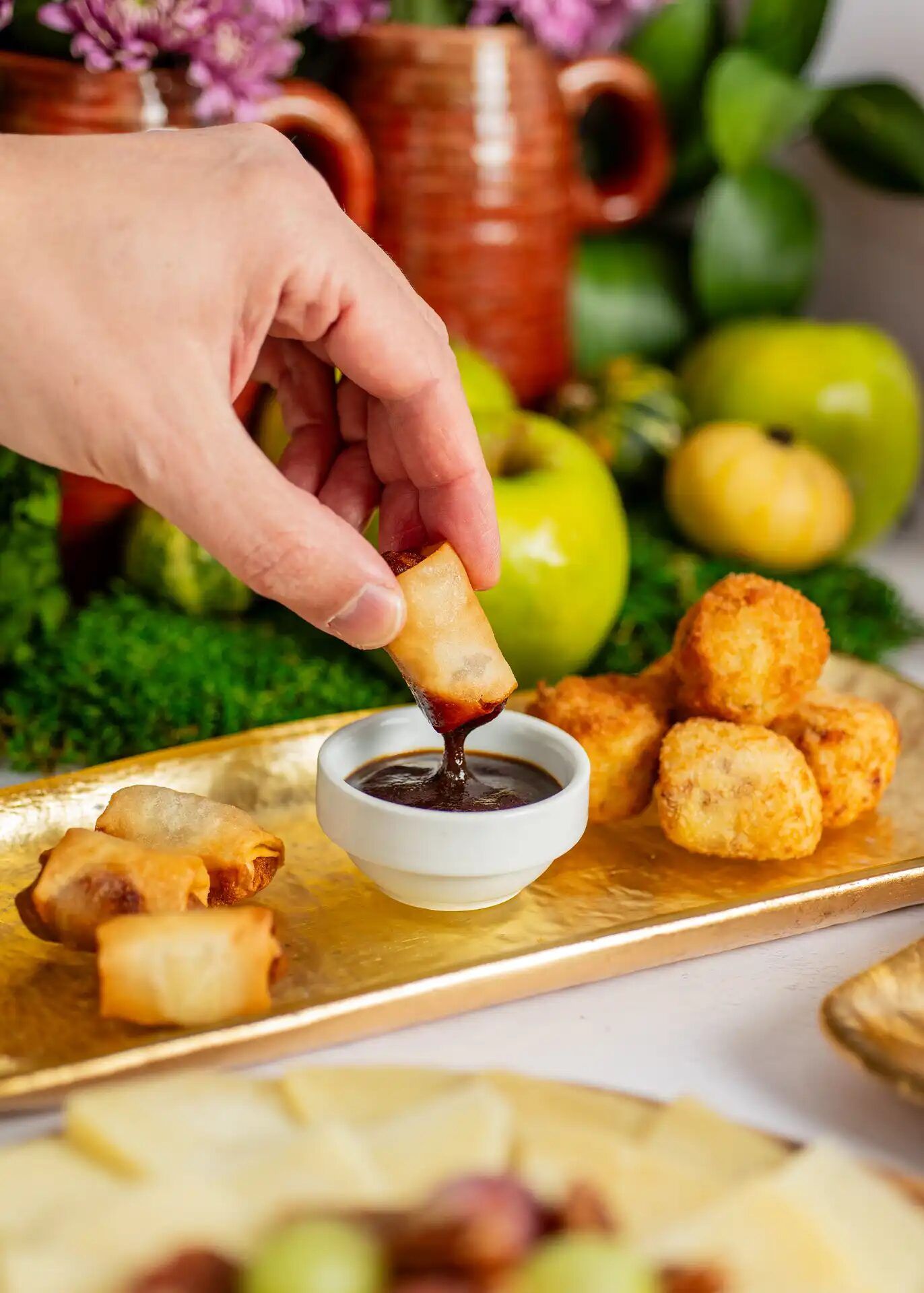Hand dipping a crispy roll into sauce next to croquettes, a María Lluch catering appetiser in Madrid