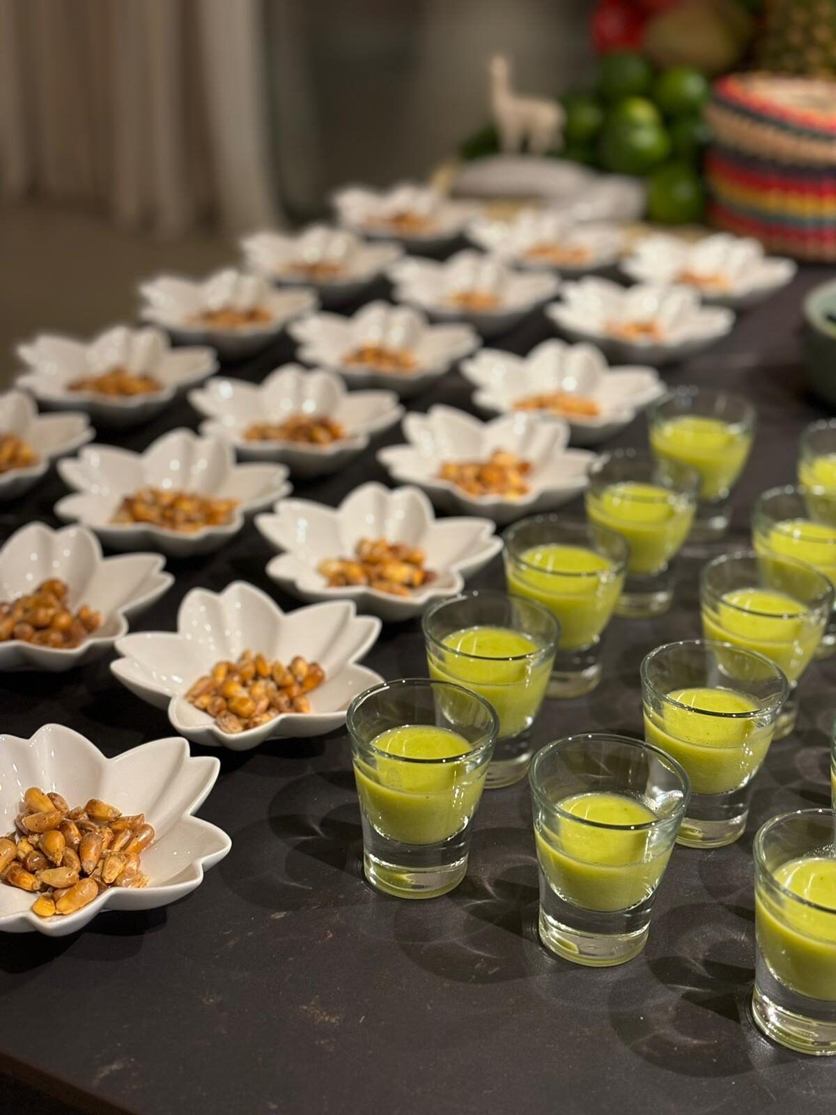 Peruvian live cooking with toasted corn and shot glasses of green cream served on a table, María Lluch catering in Madrid
